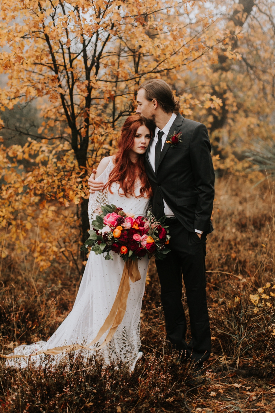 orange fall leaves in the woods. bride and groom cuddling in the woods