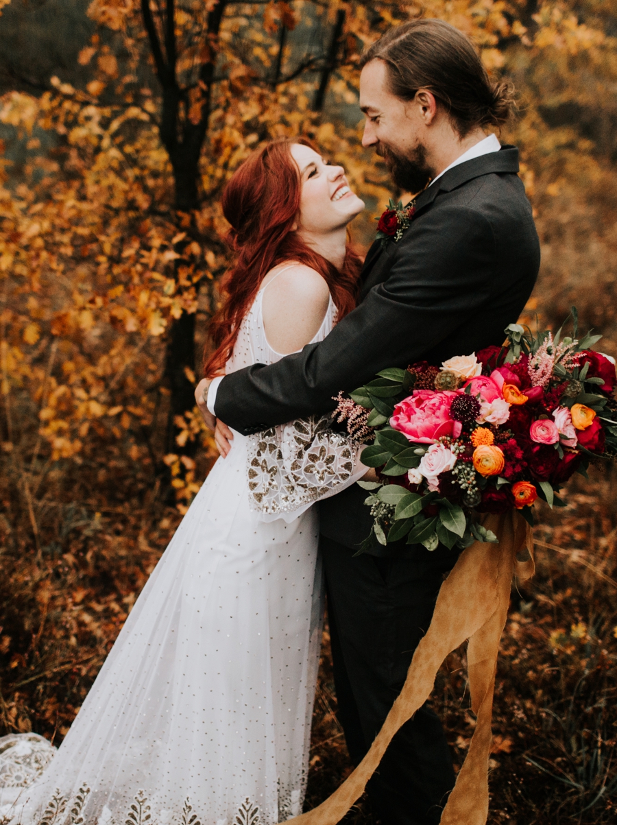 bride and groom natural posing. in love couple in the woods with an orange and maroon fall wedding palette